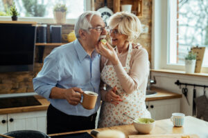 happy senior man embracing his wife while she is cooking feeding him kitchen